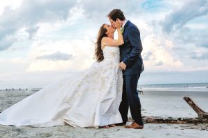 Married couple kissing on the beach in their wedding attire