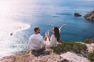 A couple in love celebrates their engagement on the seashore. A beautiful couple drinks champagne by the sea. Honeymoon trip. Lovers on the beach. Wedding travel. Couple on vacation. Copy space