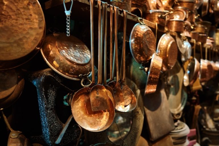 Copper handicrafted jugs, plates and other tableware hanging in a traditional middle eastern market. Brass tableware shop